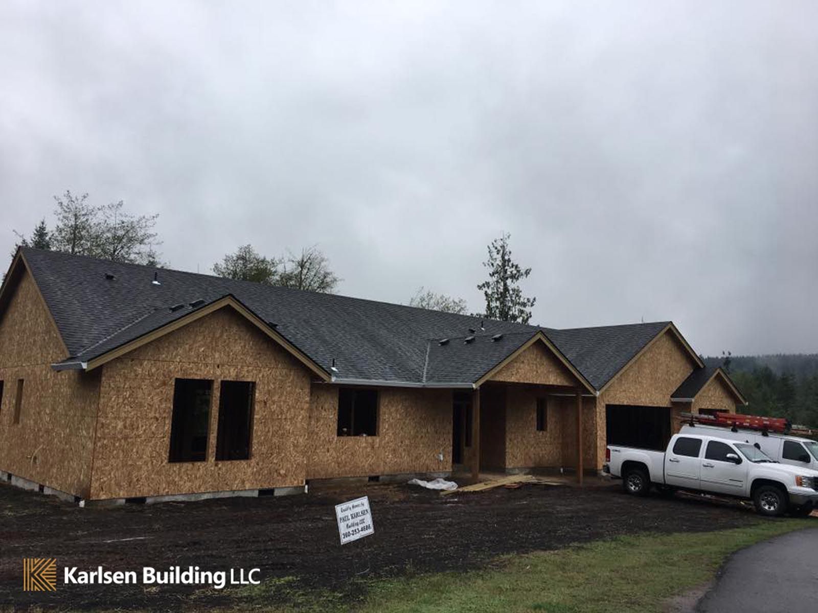 A white truck is parked in front of a house under construction.