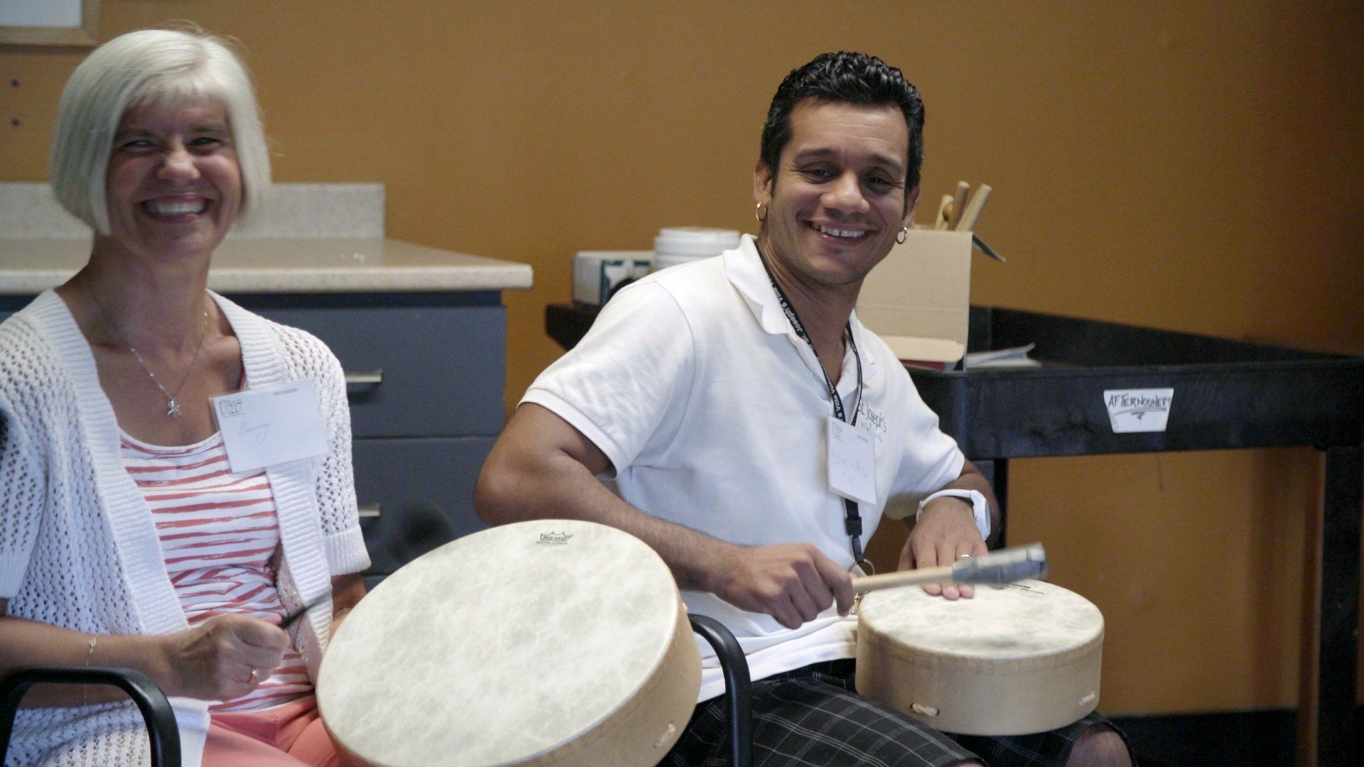 A man and a woman are playing drums and smiling for the camera