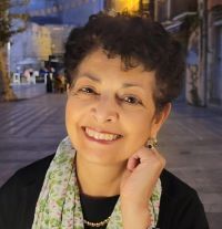 Smiling woman with short dark hair, wearing a scarf, outdoors at night.
