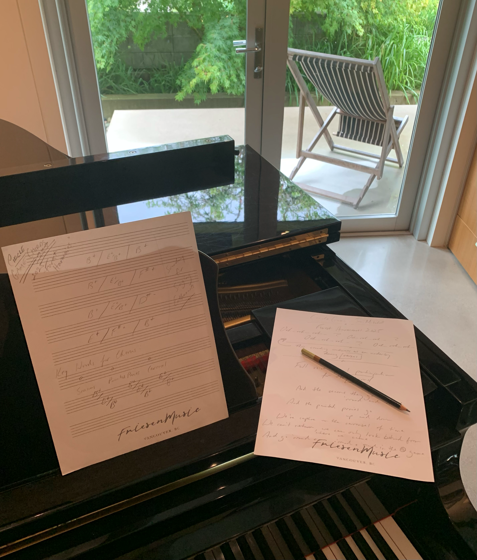 Sheet music and pencil on a piano. Outside view of chair and greenery.