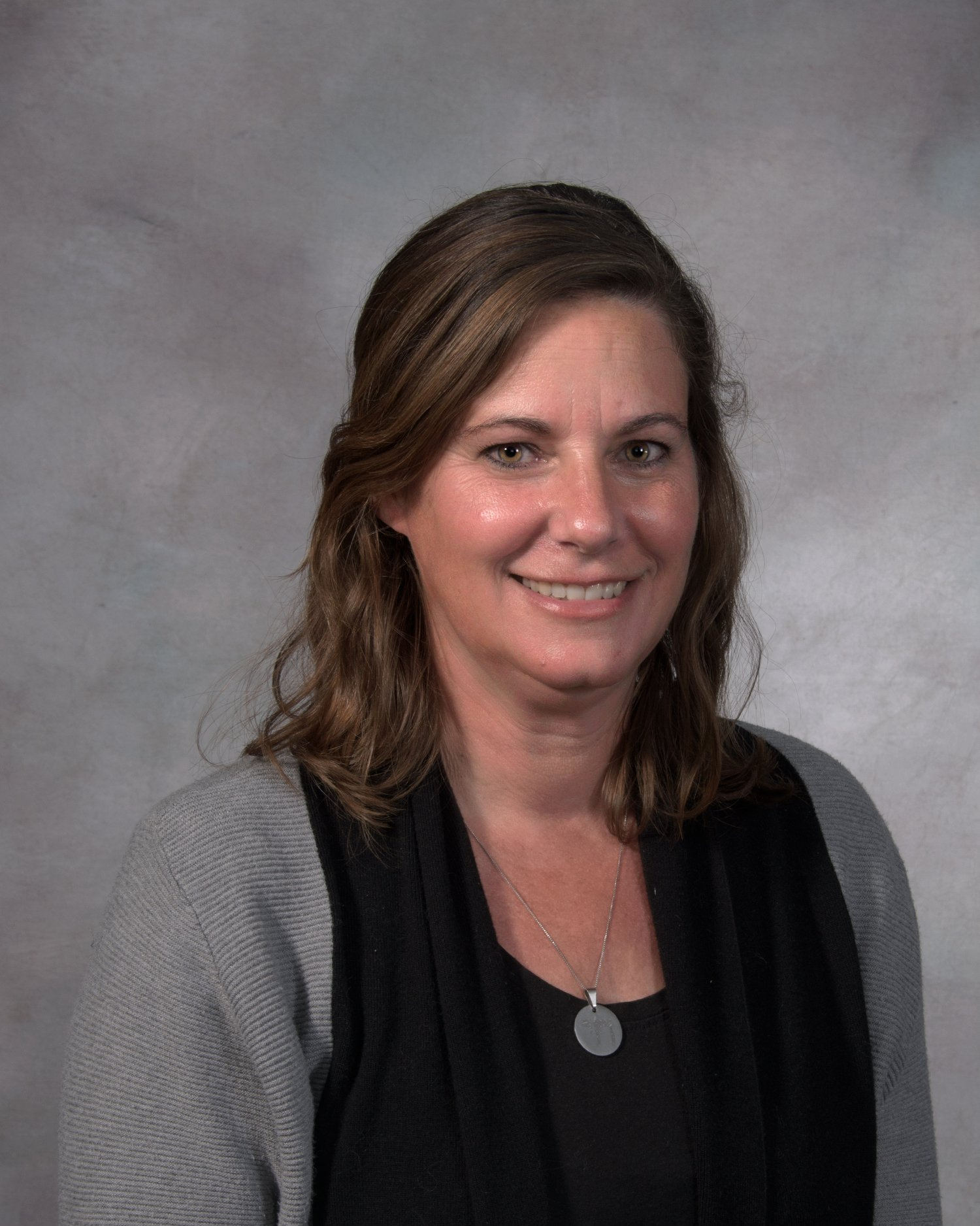 A woman wearing a black shirt and a gray sweater is smiling for the camera.