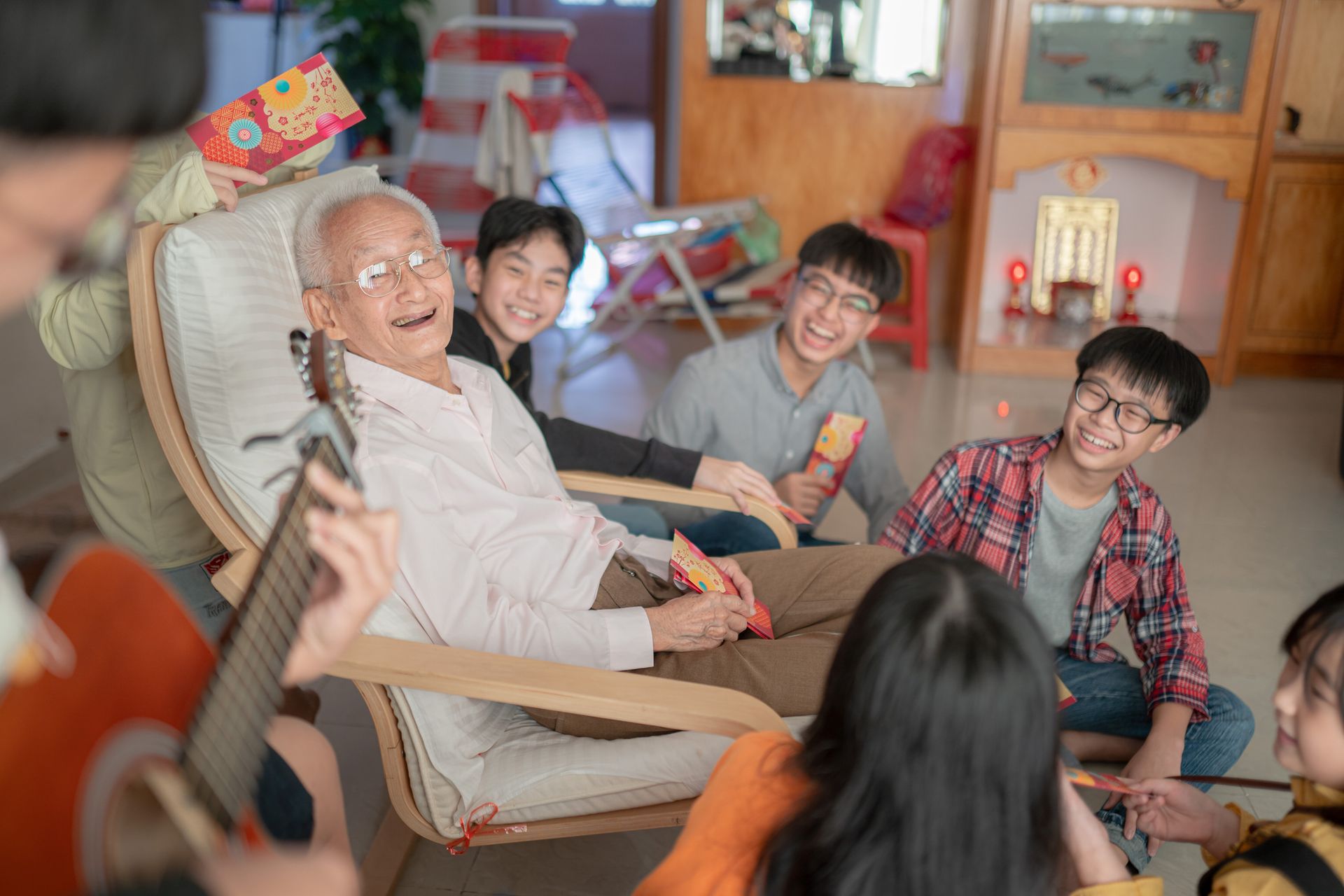 A group of people are sitting around a man in a chair playing a guitar.