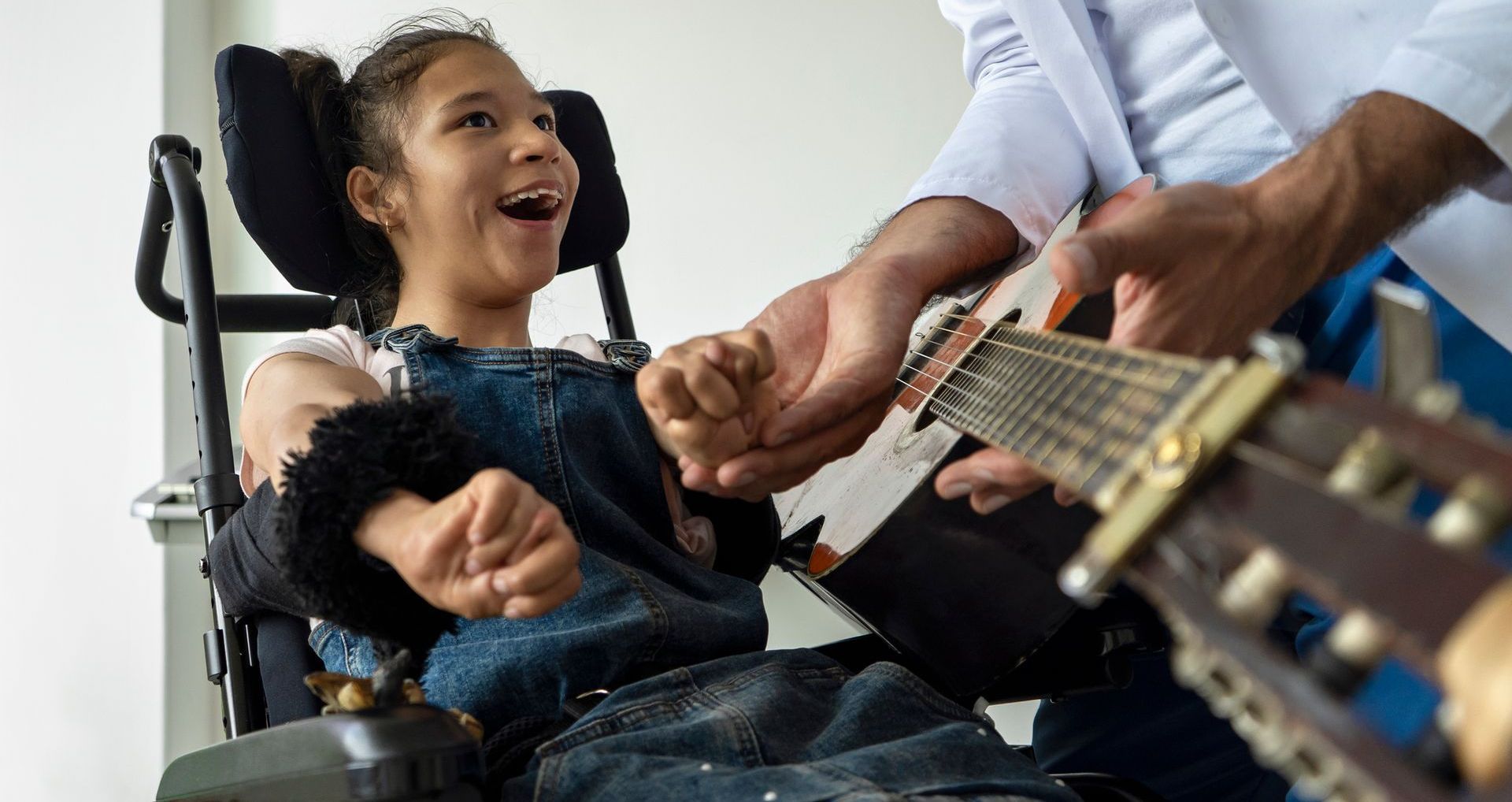 A little girl in a wheelchair is playing a guitar.