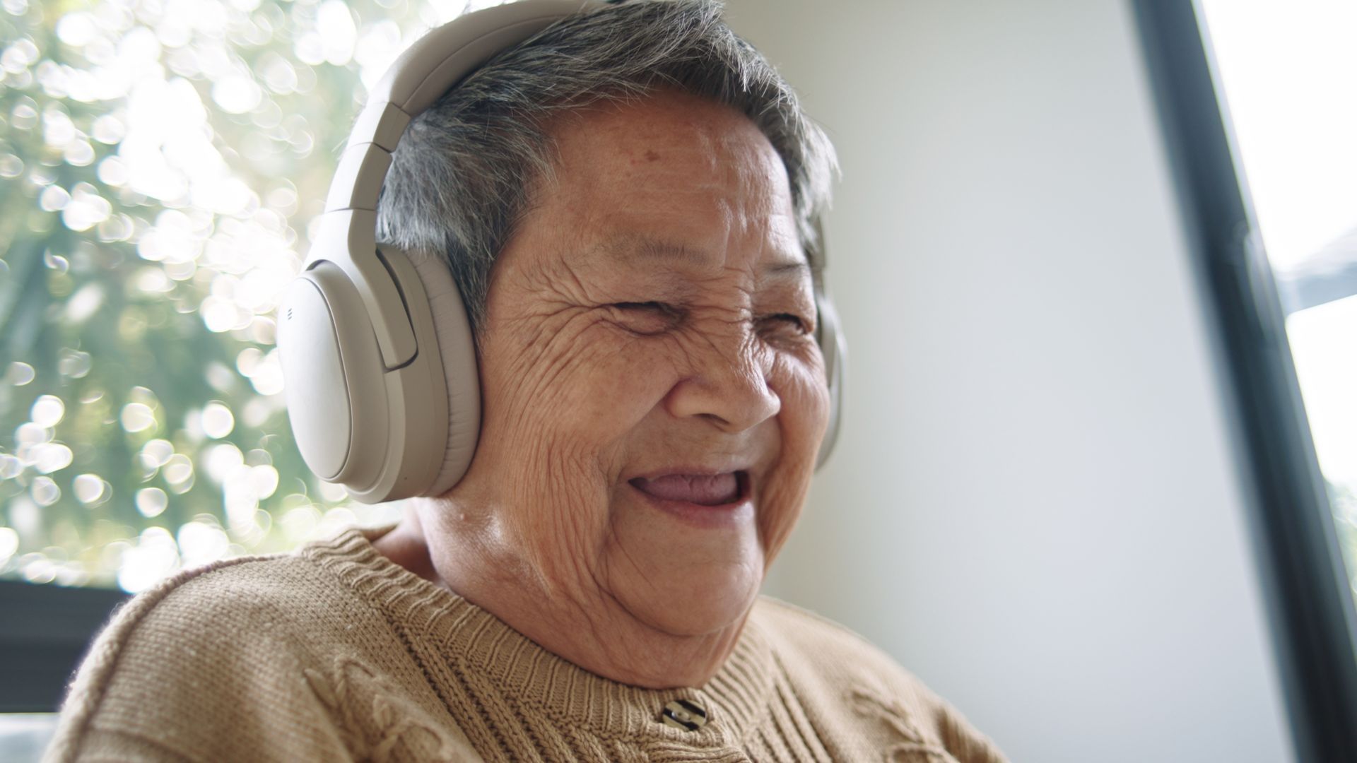 An elderly woman is wearing headphones and smiling.