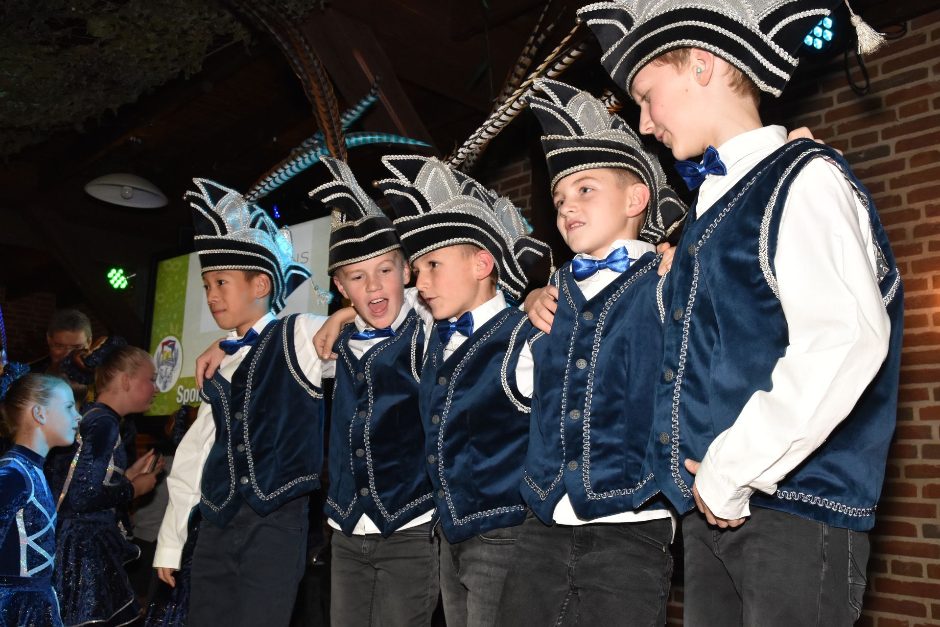 Een priester giet vloeistof in een emmer terwijl mensen in kostuum in de kerk toekijken.
