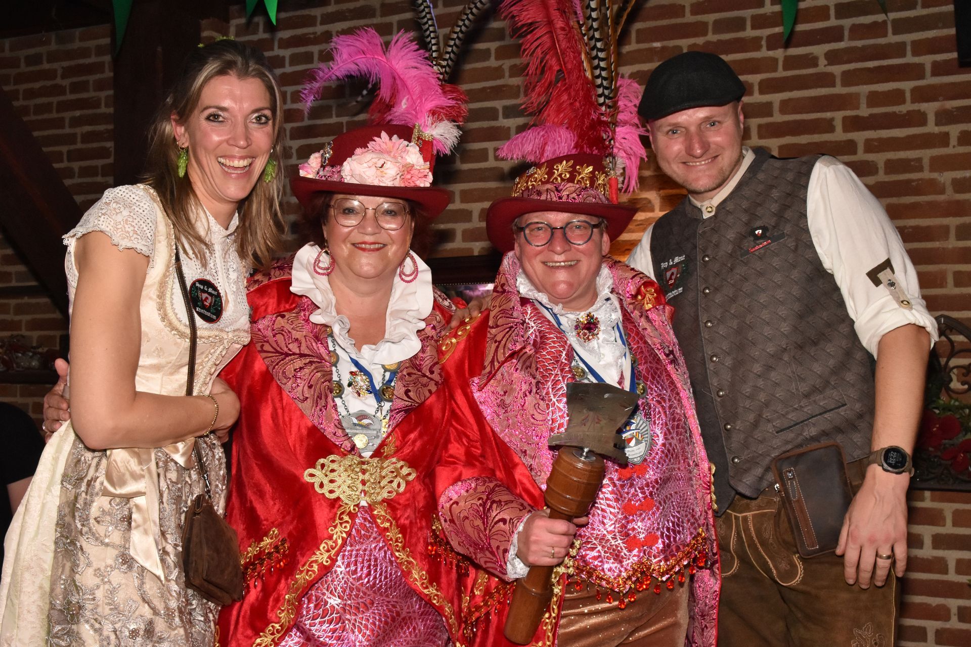 Mensen in feestelijke blauw-groene kostuums spelen een spel rond een tafel. Een vrouw kijkt glimlachend van achteren toe.
