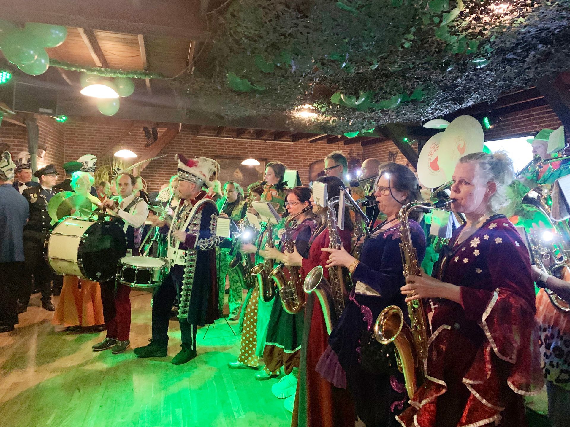 Een band in kostuum speelt muziek tijdens een evenement, met drums, saxofoons en kleurrijke outfits.
