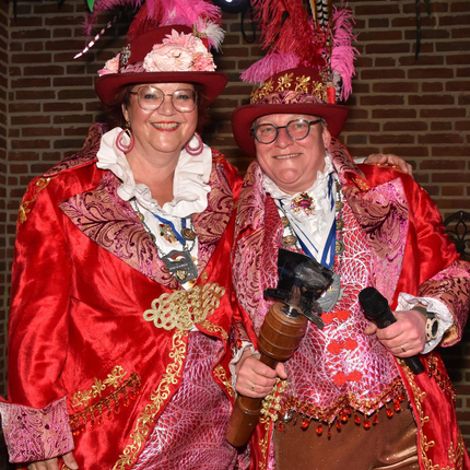 Een kantoorgang met kamers met glazen wanden, beige tapijt en twee stoelen tegenover een klein tafeltje.