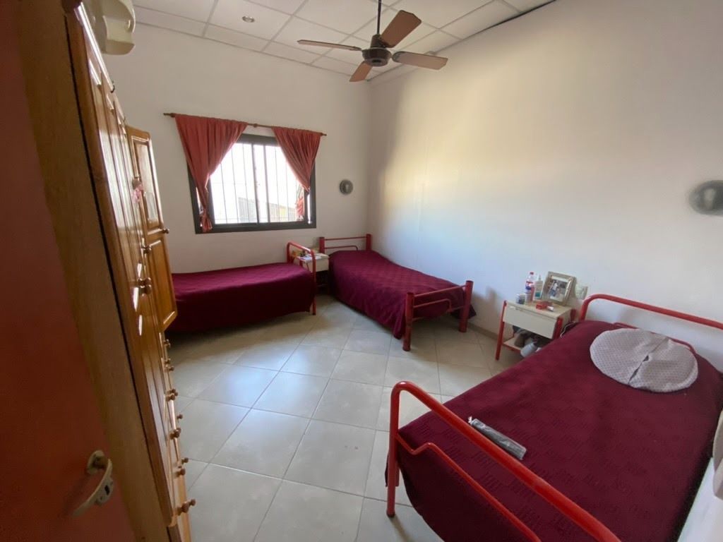 Un dormitorio con tres camas individuales con colchas rojas, una ventana con cortinas rojas y un ventilador de techo.