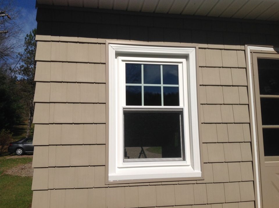 A window with white trim on a tan shingled wall, next to a tan door. Sunlight reflects in the glass.