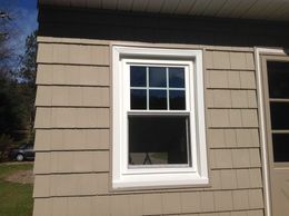 A white-framed window on a beige shingled house. Sunlight reflects in the glass. A door is to the right.