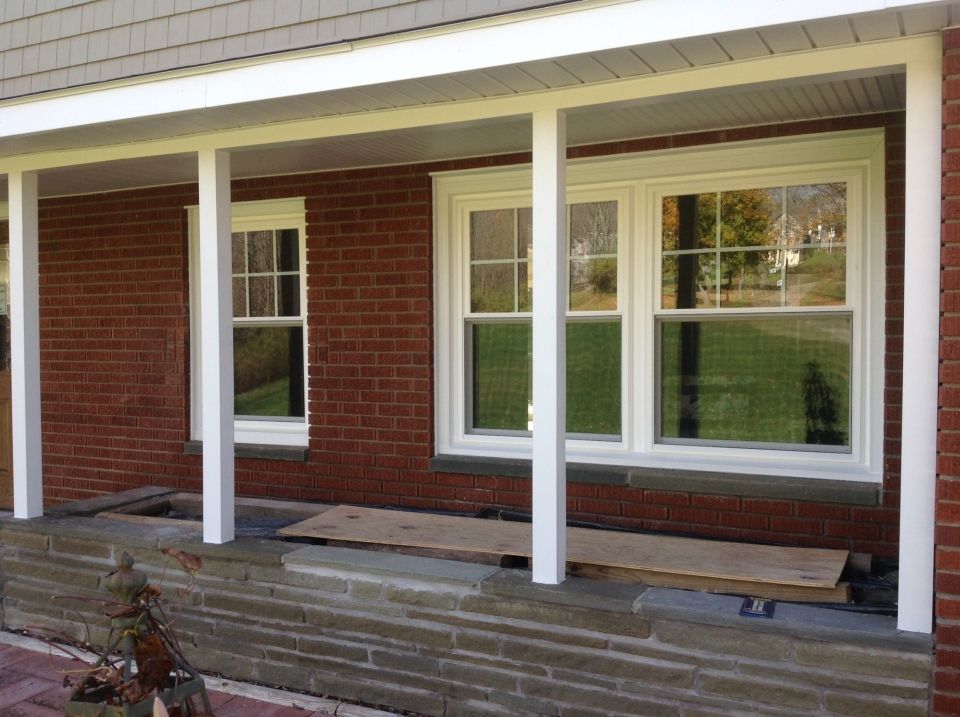 Exterior view of a brick building with white columns and windows under a porch overhang. Boards are placed on a stone ledge.