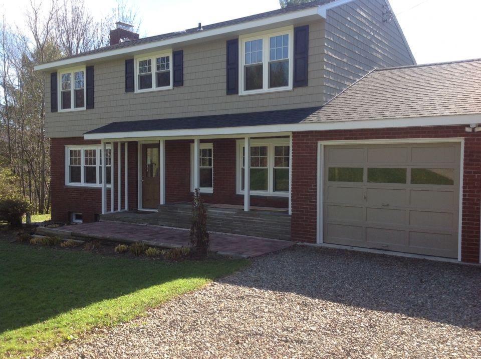 Two-story house with beige siding, red brick accents, a beige garage door, and a brick porch and driveway.