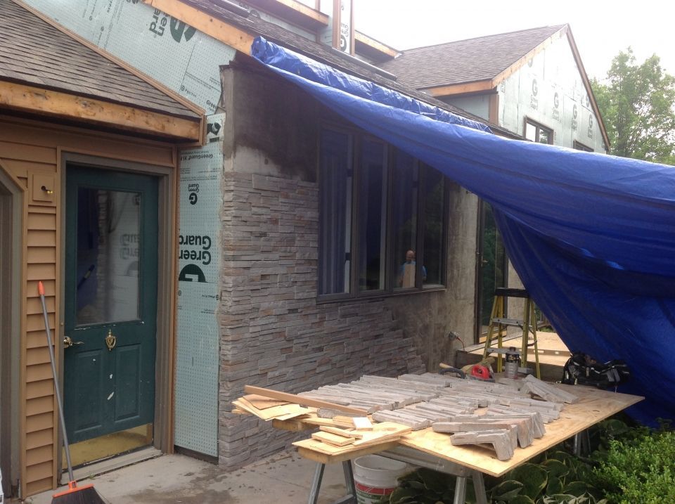 Construction site with brickwork partially covering a building. A blue tarp protects the unfinished stonework.