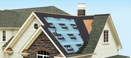 A partially re-roofed house, showcasing roofing layers and shingles. Blue underlayment is visible.
