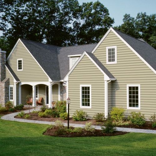 Green-sided house with white trim and a dark gray roof. A walkway leads to the front door, surrounded by green grass and landscaping.