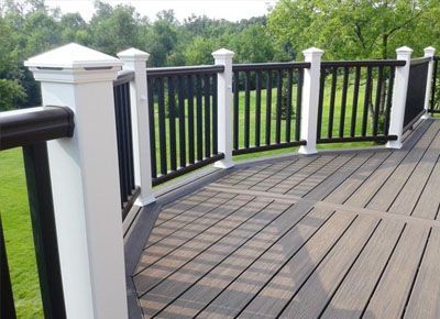 Composite deck with white posts, black railings, and brown composite boards, overlooking a green lawn and trees.