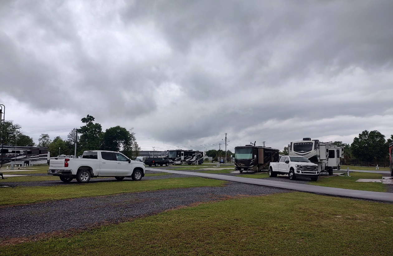 RV park on a cloudy day. RVs and pickup trucks are parked on grass and gravel.