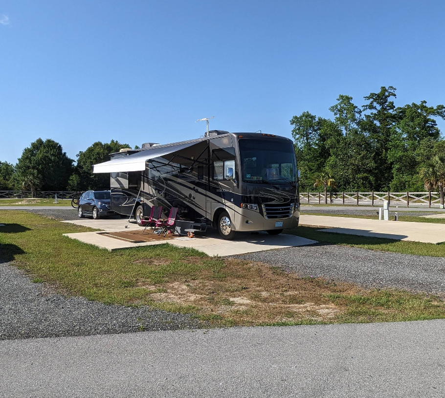 RV parked on gravel campsite with awning extended on a sunny day.
