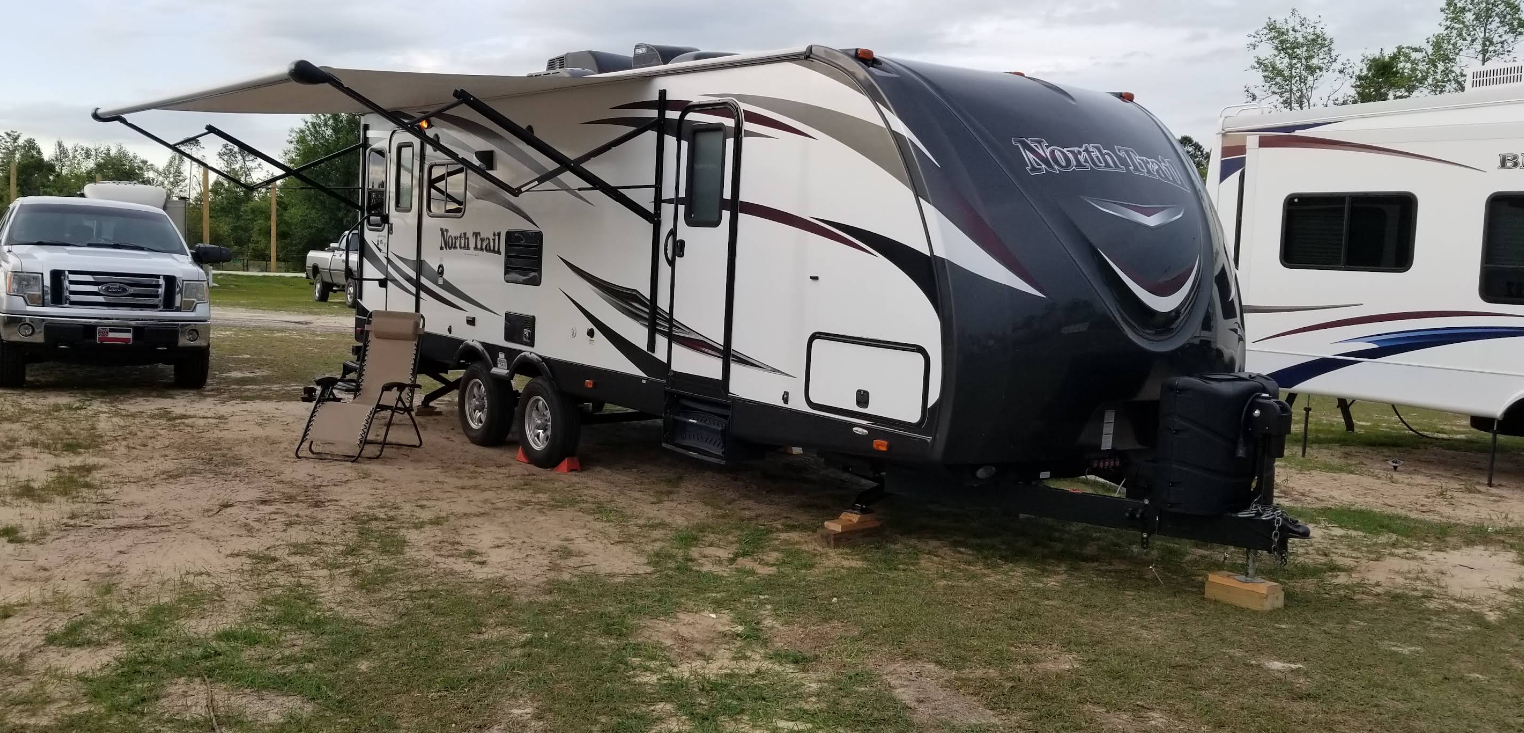 RV parked on a grassy lot with the awning extended. A white truck sits in front of the RV.
