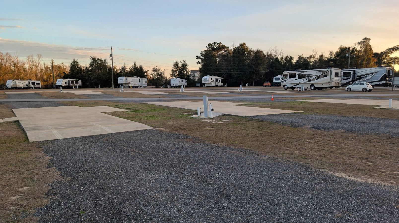 RV park with gravel driveways, concrete pads, and parked RVs under a blue sky.