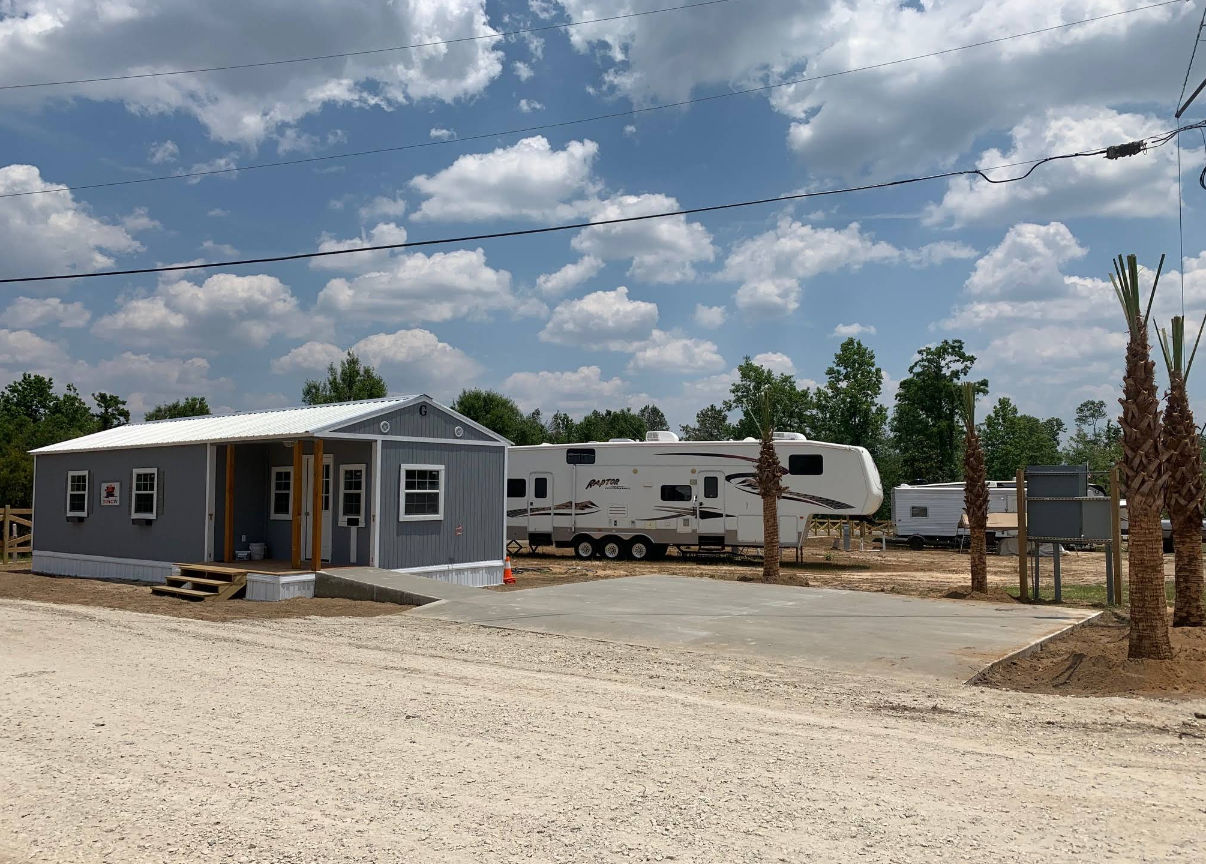 Gray building and RVs parked on gravel under a cloudy sky.