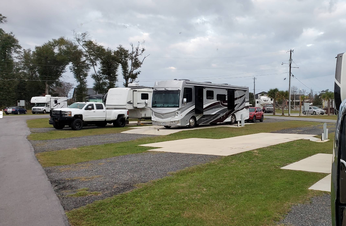 RV park with vehicles parked on gravel and grass under cloudy skies.