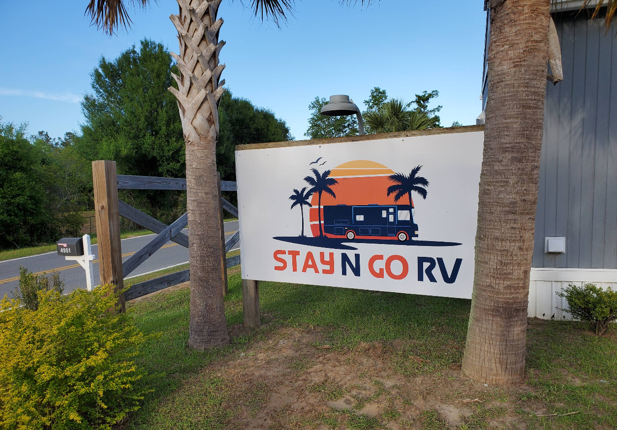 Sign for Stay N Go RV park with RV graphic, palm trees, and blue sky.