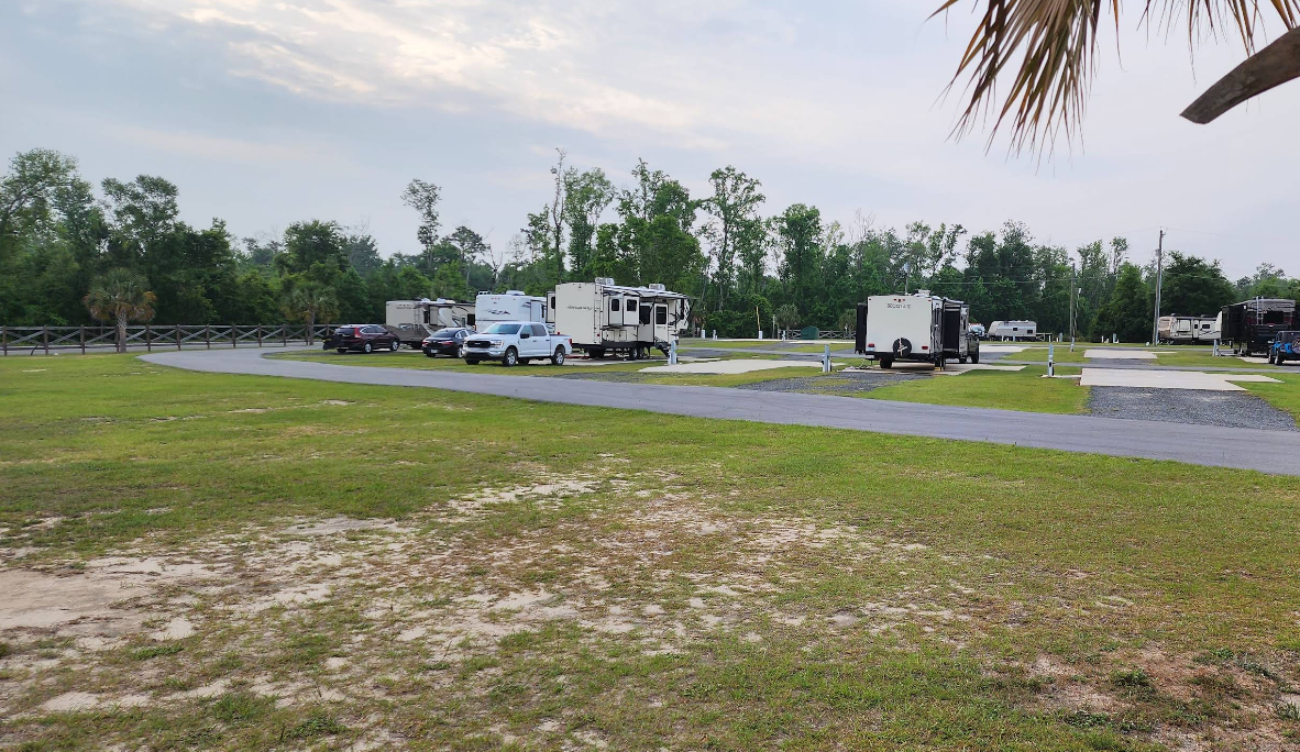 RV campground with parked RVs on gravel pads, grassy area, and trees.
