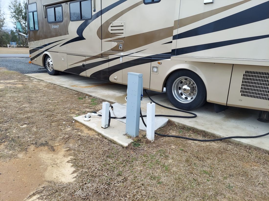 RV parked at campsite with hookups for water, electric, and sewer. Brown, tan, and black exterior.