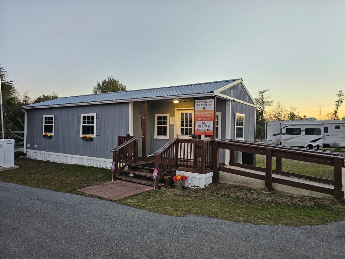 A blue-gray building with a wooden porch and ramp, likely an office or welcome center at a campground.