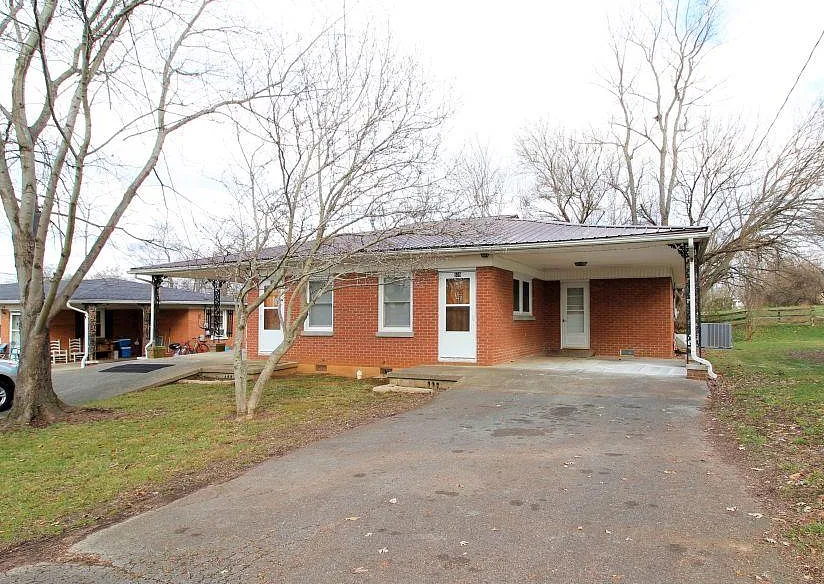Red brick house with carport and driveway on a grassy lot, bare trees.