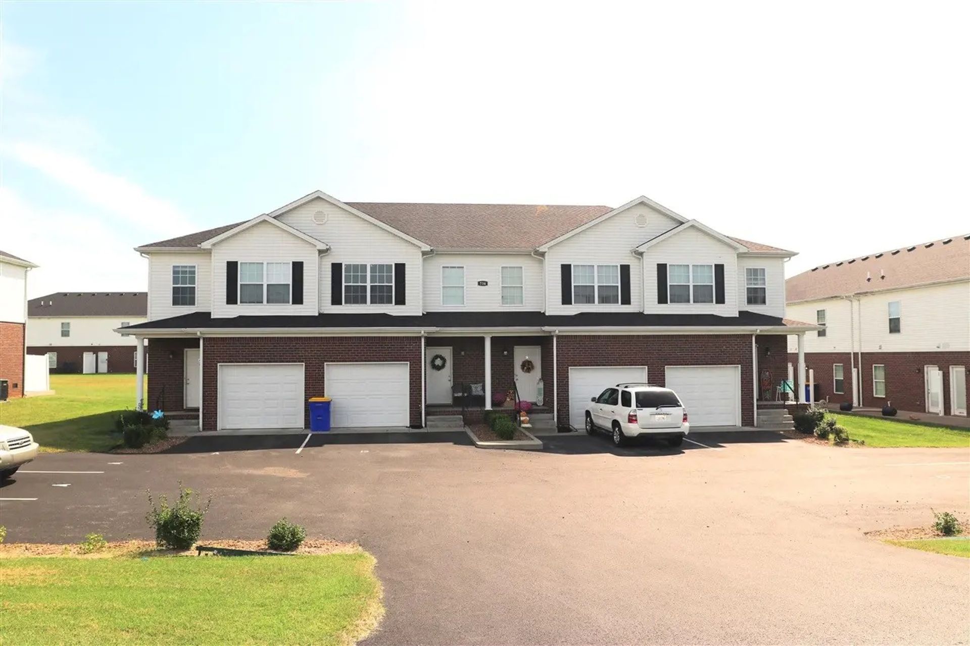 Two-story brick and white duplex with garages. White SUV parked in front of the right unit.