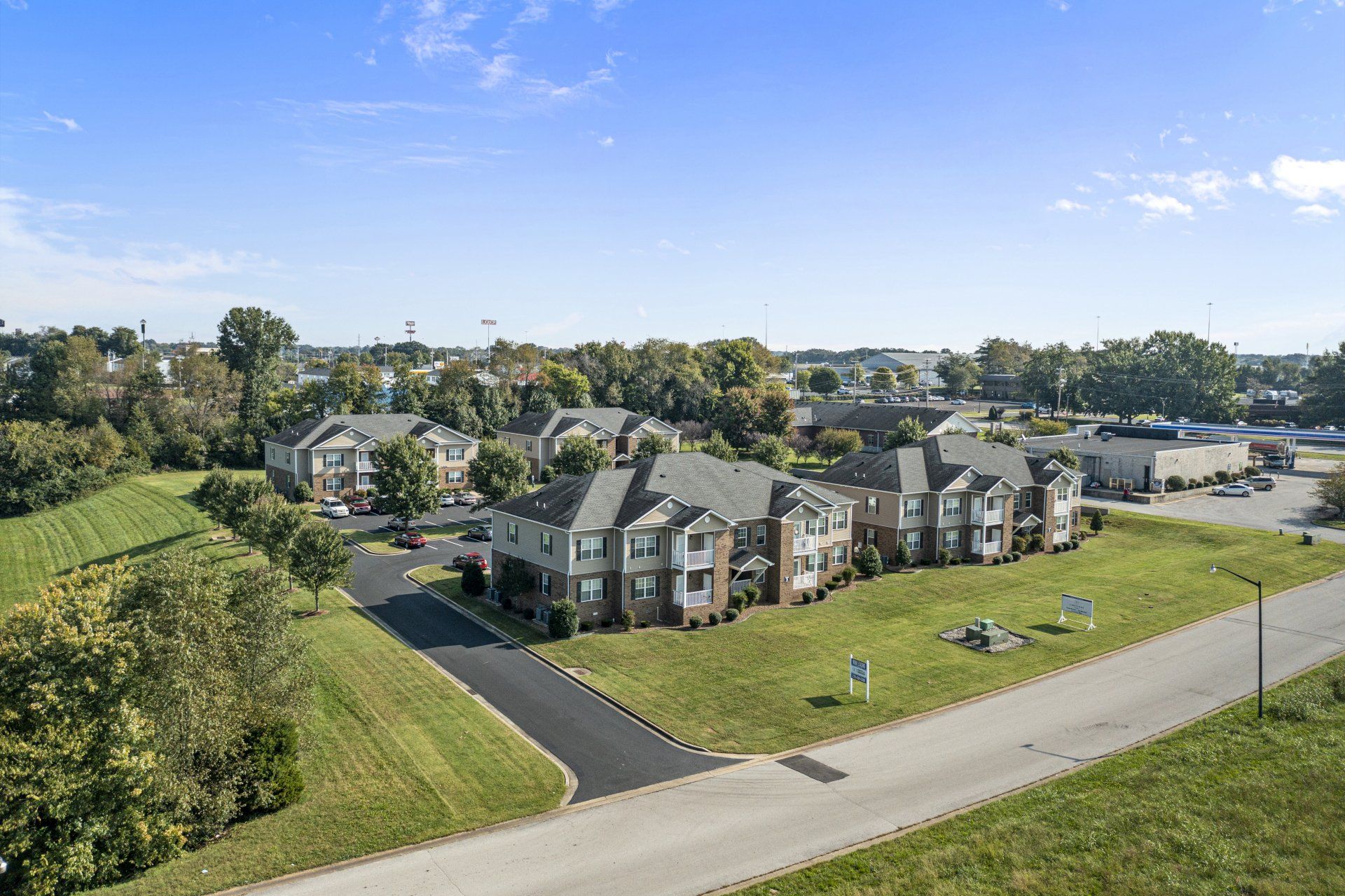 Aerial view of apartment buildings with dark green roofs and surrounding greenery under a blue sky.