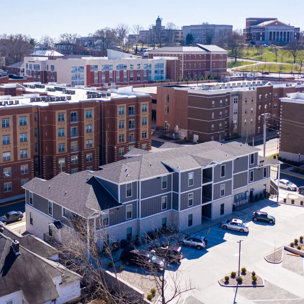Aerial view of modern gray and brown apartment buildings near a college campus.