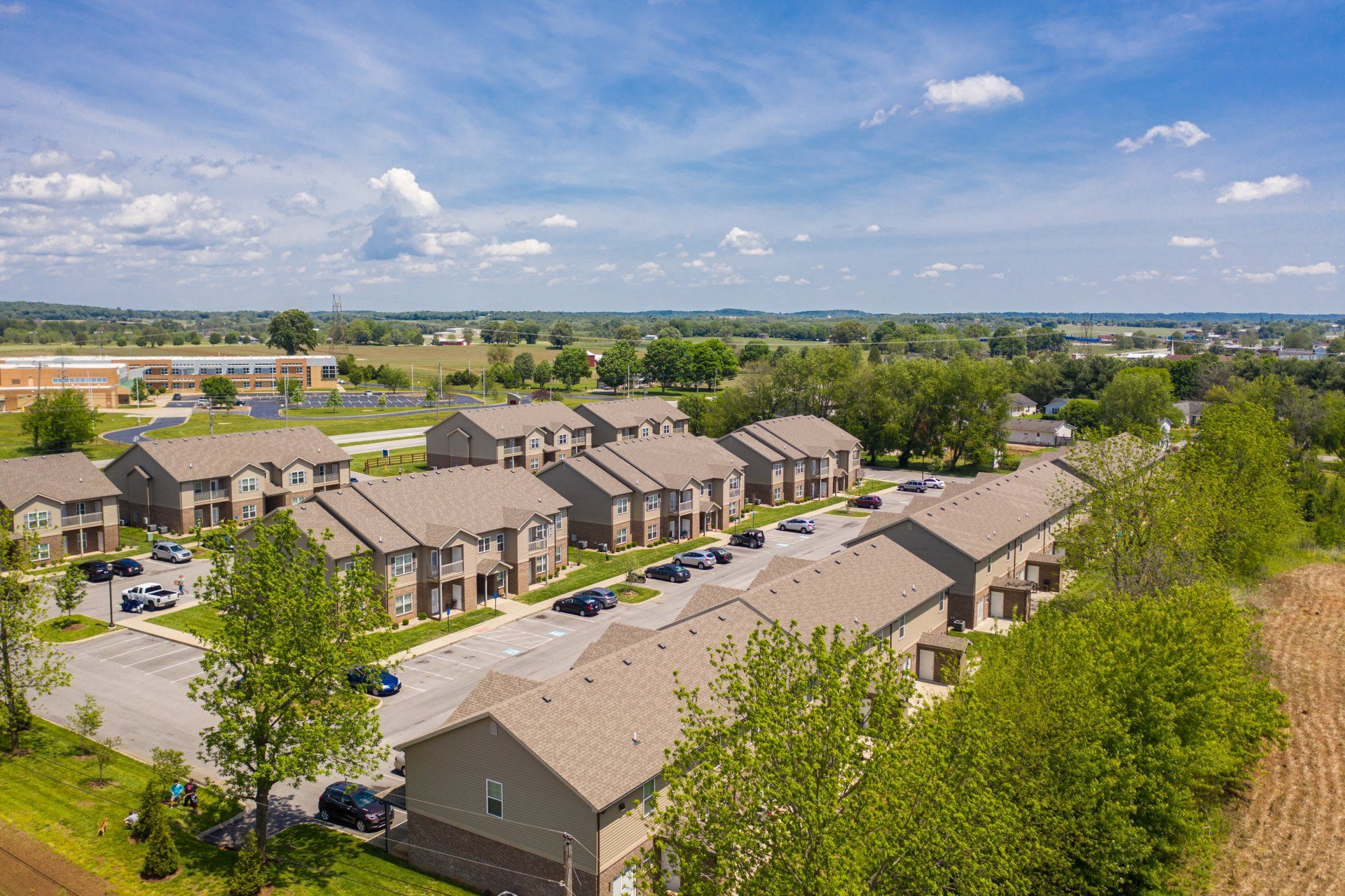 Aerial view of tan apartment buildings with a blue sky and green trees.