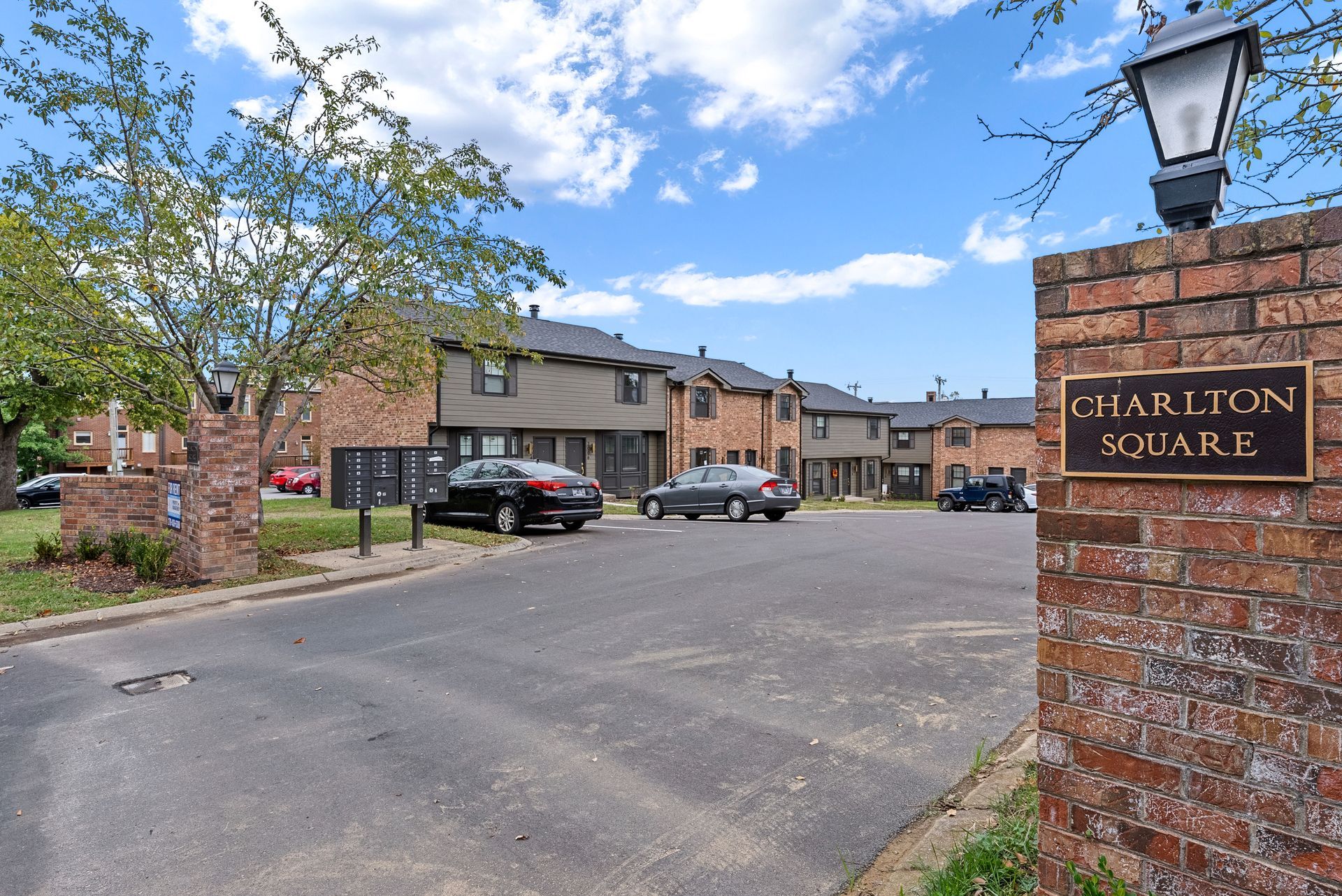 Charlton Square apartment complex entrance; brick columns with sign, cars parked on asphalt.
