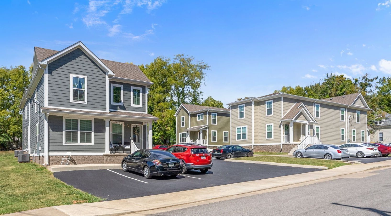 Apartment buildings with cars parked in front on a sunny day.