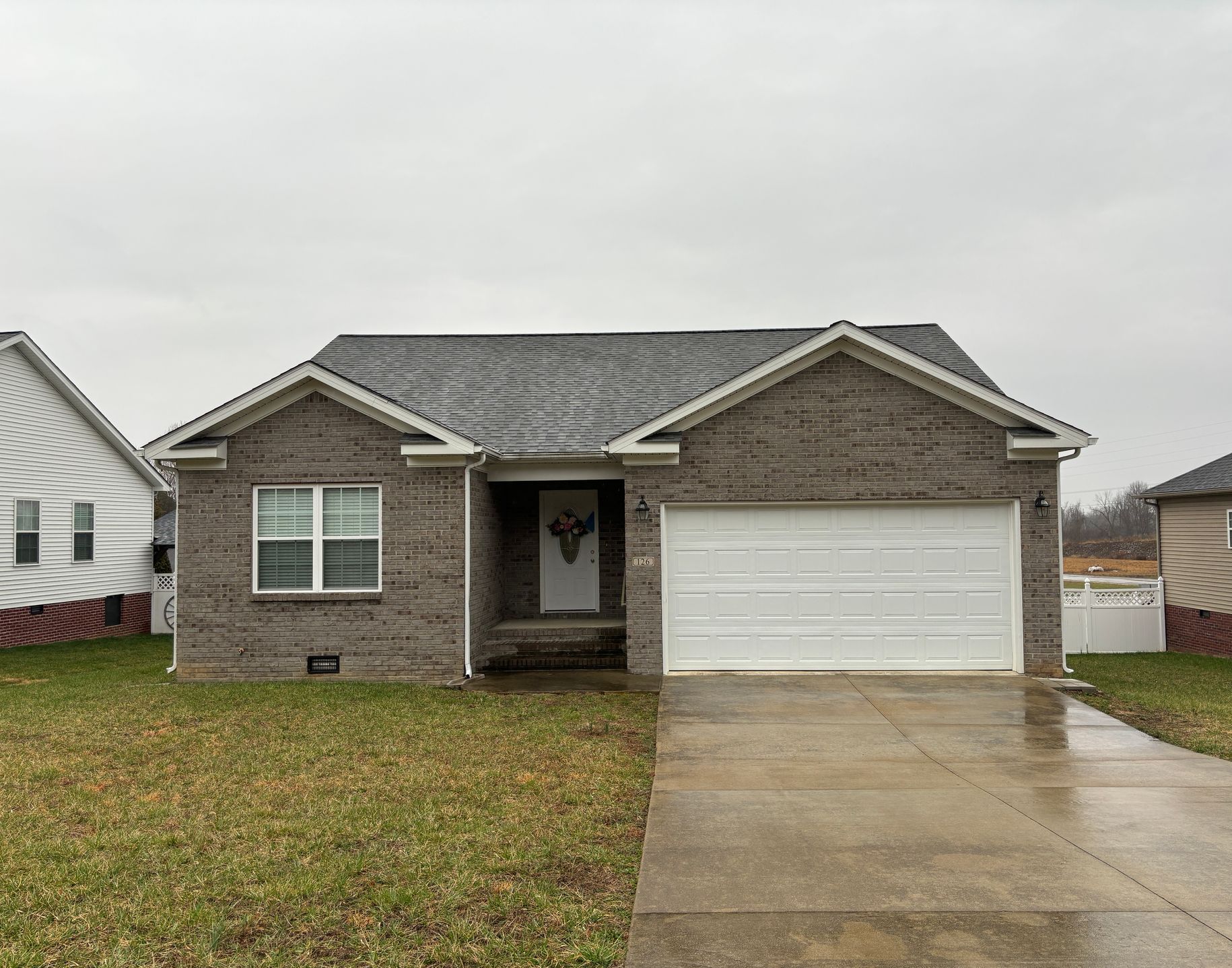 Brick house with a white garage door and gray roof on a cloudy day.