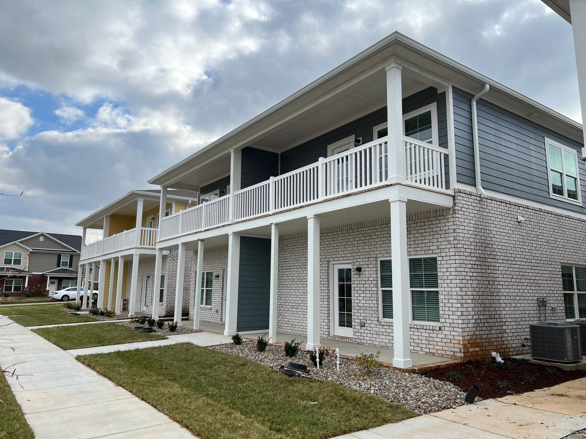 Row of multi-story townhouses with light brick and dark gray siding, white balconies, and cloudy sky.