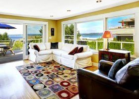 Bright living room with white sofas, colorful rug, and ocean views through large windows