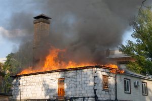 House engulfed in flames with thick smoke rising from the roof and chimney.