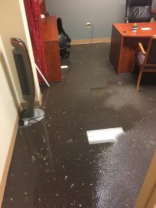 Flooded office floor with water pooled across the carpet near desks and a chair