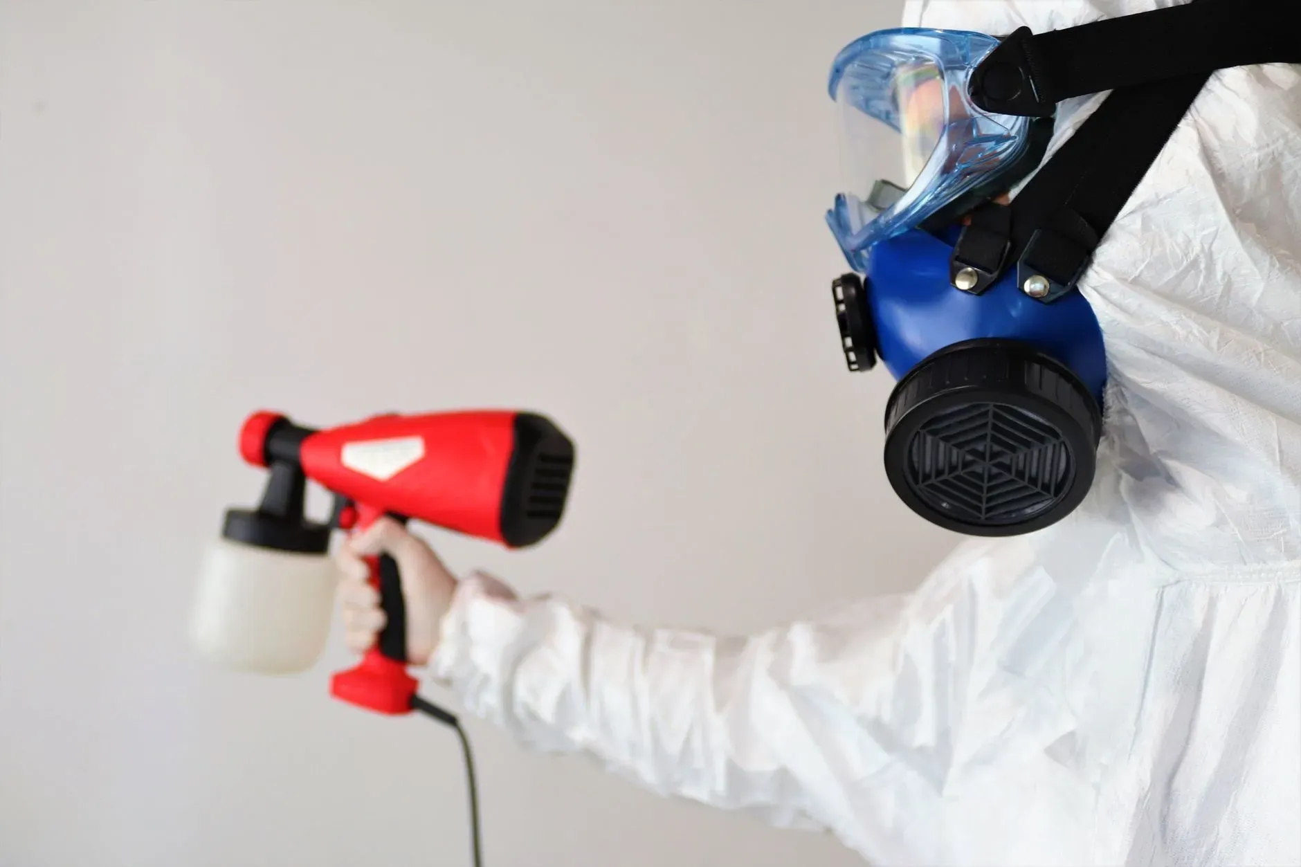 Person in white protective suit spraying disinfectant with red and blue sprayers