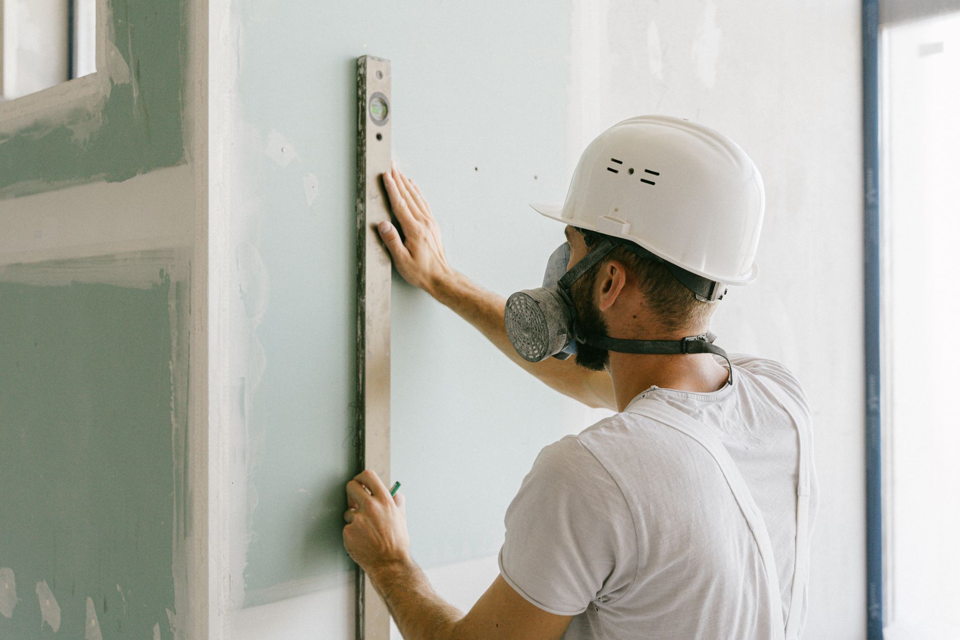 Worker in a white hard hat measures a wall with a level during interior renovation