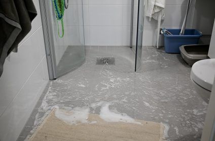 Small bathroom with a wet, damaged gray floor and open glass shower doors.