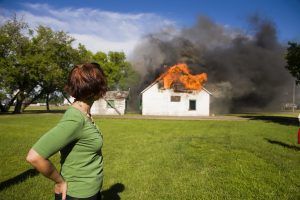 House on fire with thick smoke while a person stands watching from a grassy yard