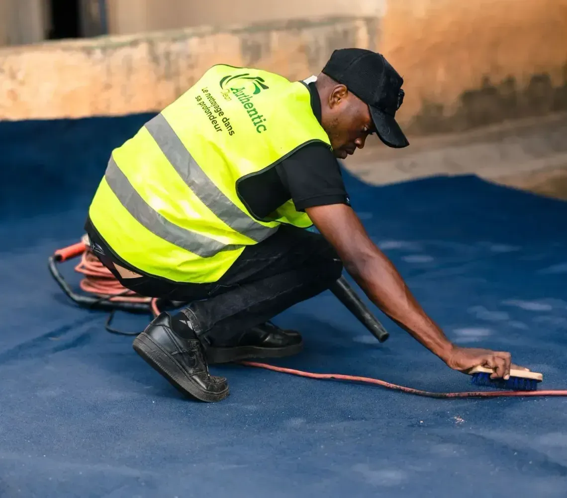 Worker in a neon safety vest kneeling to spread blue coating on a floor with a trowel.