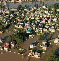 Aerial view of a flooded neighborhood with submerged houses and muddy water surrounding roads and trees