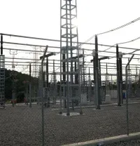 Electrical substation with metal towers, fencing, and warning signs on a gravel lot